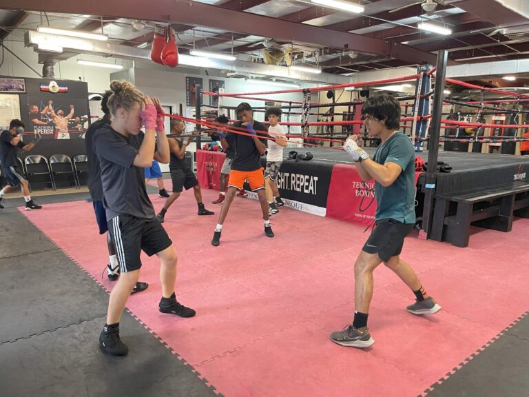 Four people sparring in a boxing gym ring.
