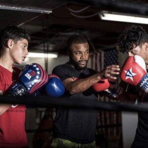 A coach trains two young boxers in a gym.